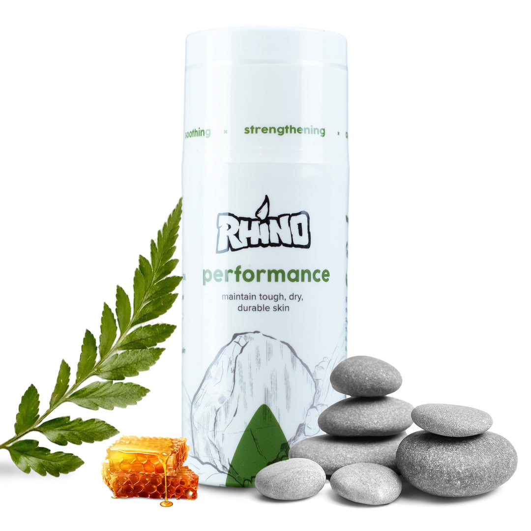 Rhino Skin Solutions Performance balm for climbers and athletes, shown with natural ingredients like honeycomb, smooth stones, and a fern leaf—ideal for maintaining tough, dry, durable skin.