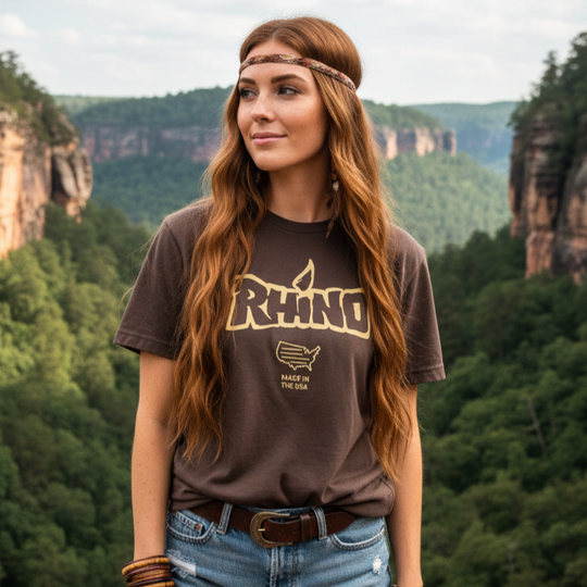Woman wearing a 'Rhino' t-shirt in a scenic outdoor setting with mountains and trees.