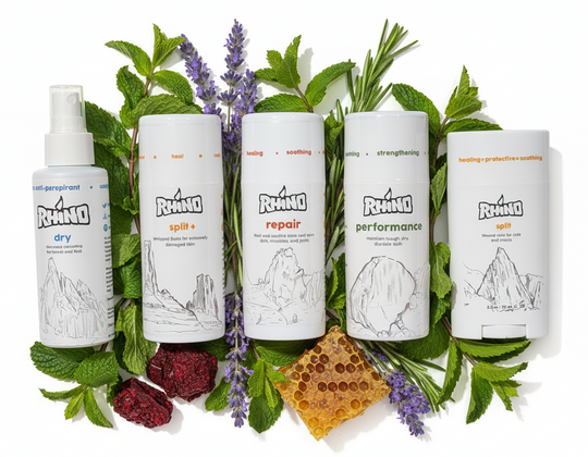 Five Rhino care product bottles surrounded by herbs and natural elements on a white background