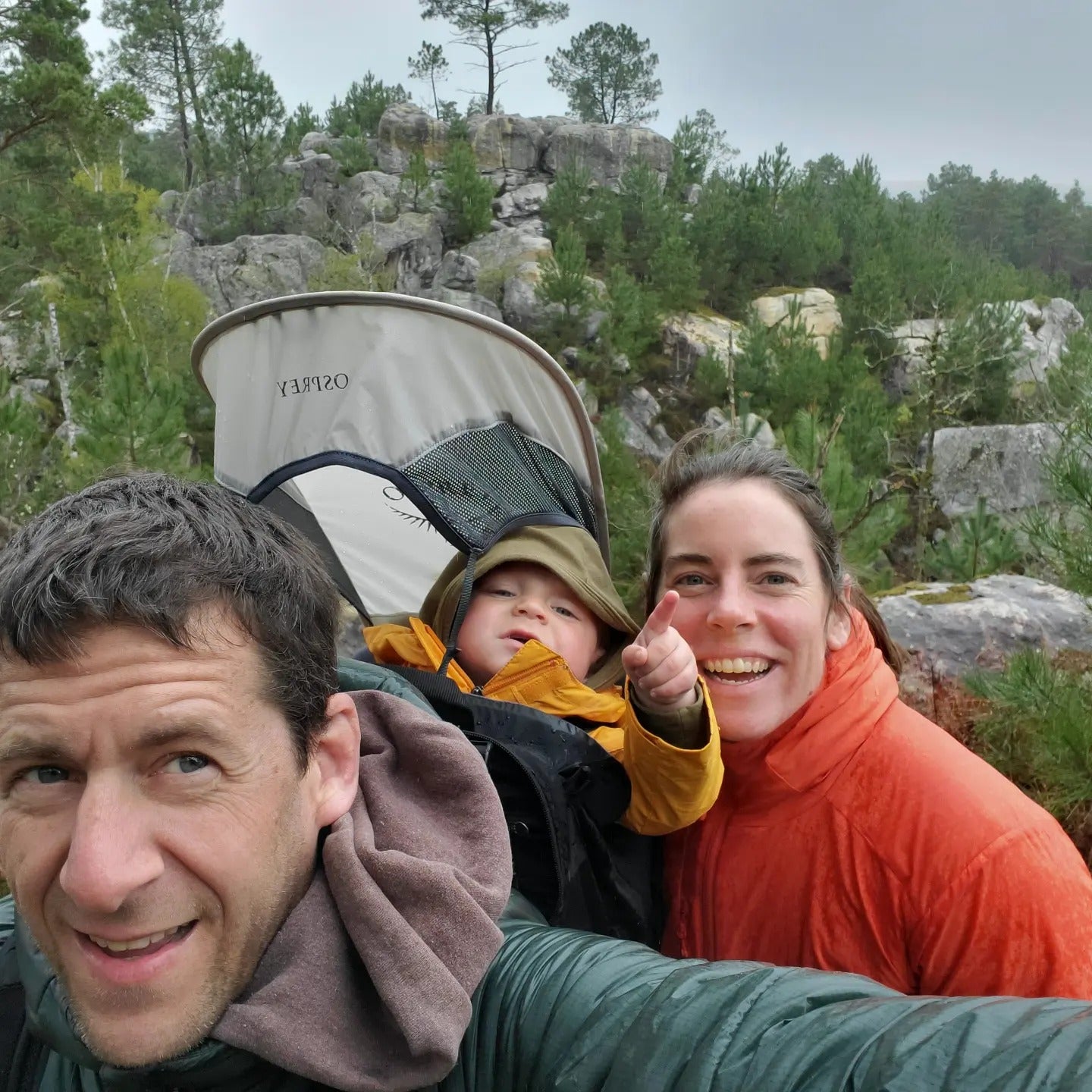 Owners of Rhino Skin Solutions with their child in Fontainebleau on a rainy day, standing near iconic boulders. The family is dressed for the weather, capturing the essence of the climbing lifestyle in an outdoor, natural setting.