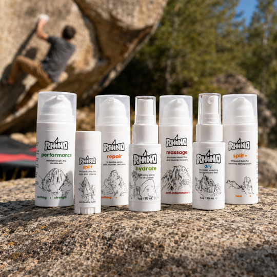 Six white Rhino brand skincare bottles and a tube arranged on a rock outdoors, with a blurred climber and trees in the background.