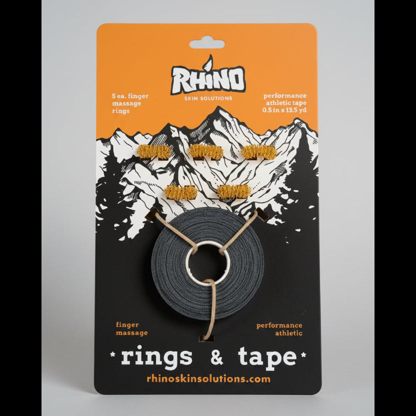 Packaged Rhino Skin Solutions finger massage rings and performance athletic tape on a wooden surface. The orange and black card shows a mountain graphic and five gold rings with a spool of dark gray tape.