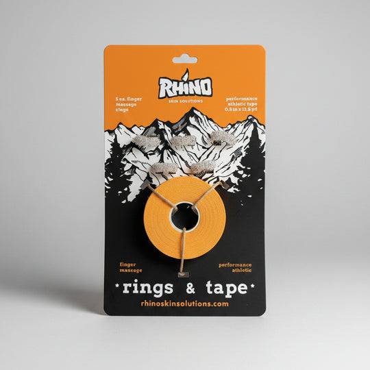 A roll of Rhino Skin Solutions performance athletic tape for finger massage and rings, mounted on its original orange and black cardboard backing card, photographed on a light wood surface.